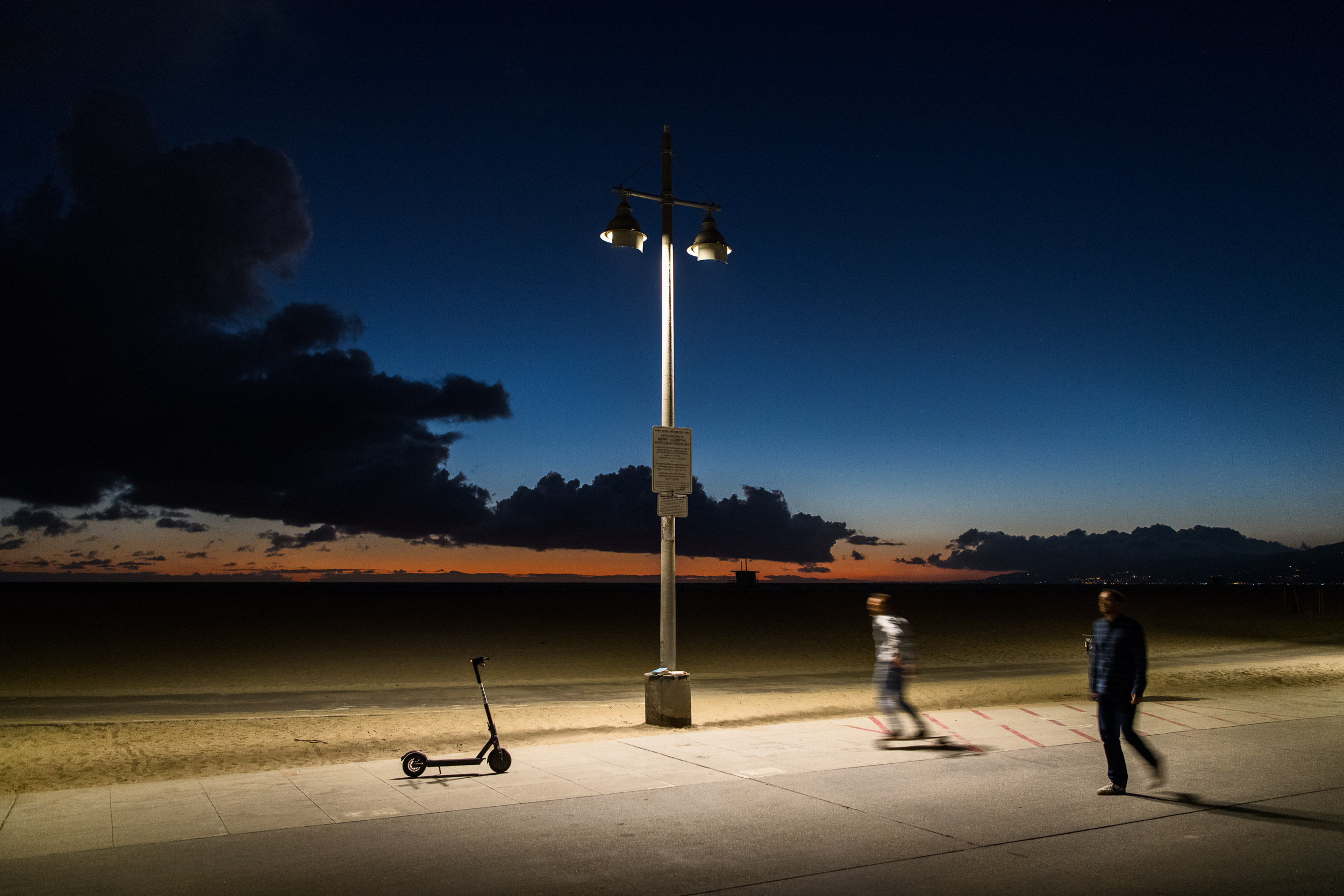Anthropomorphic Bird scooter under a street lamp at night on the Venice Beach boardwalk.