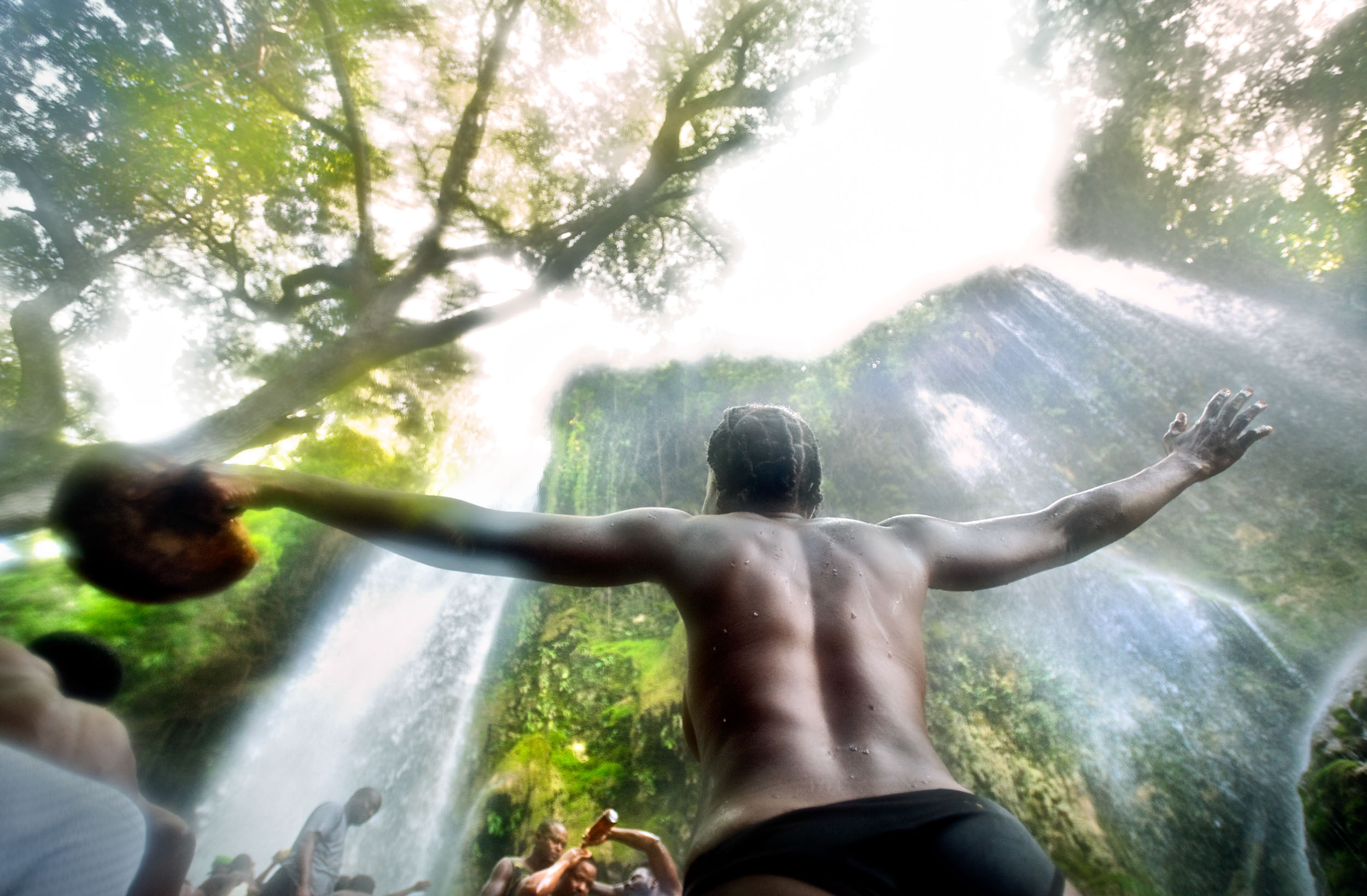 A woman raises her hands in prayer under a waterfall  during the Saut D