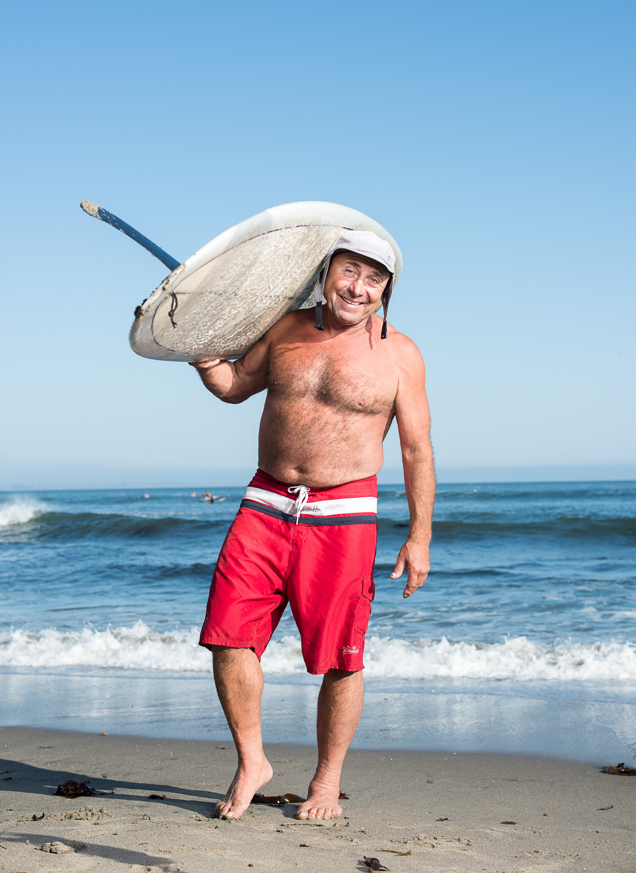 An older man surfer stands with his board on the beach in Santa Cruz, Calif.