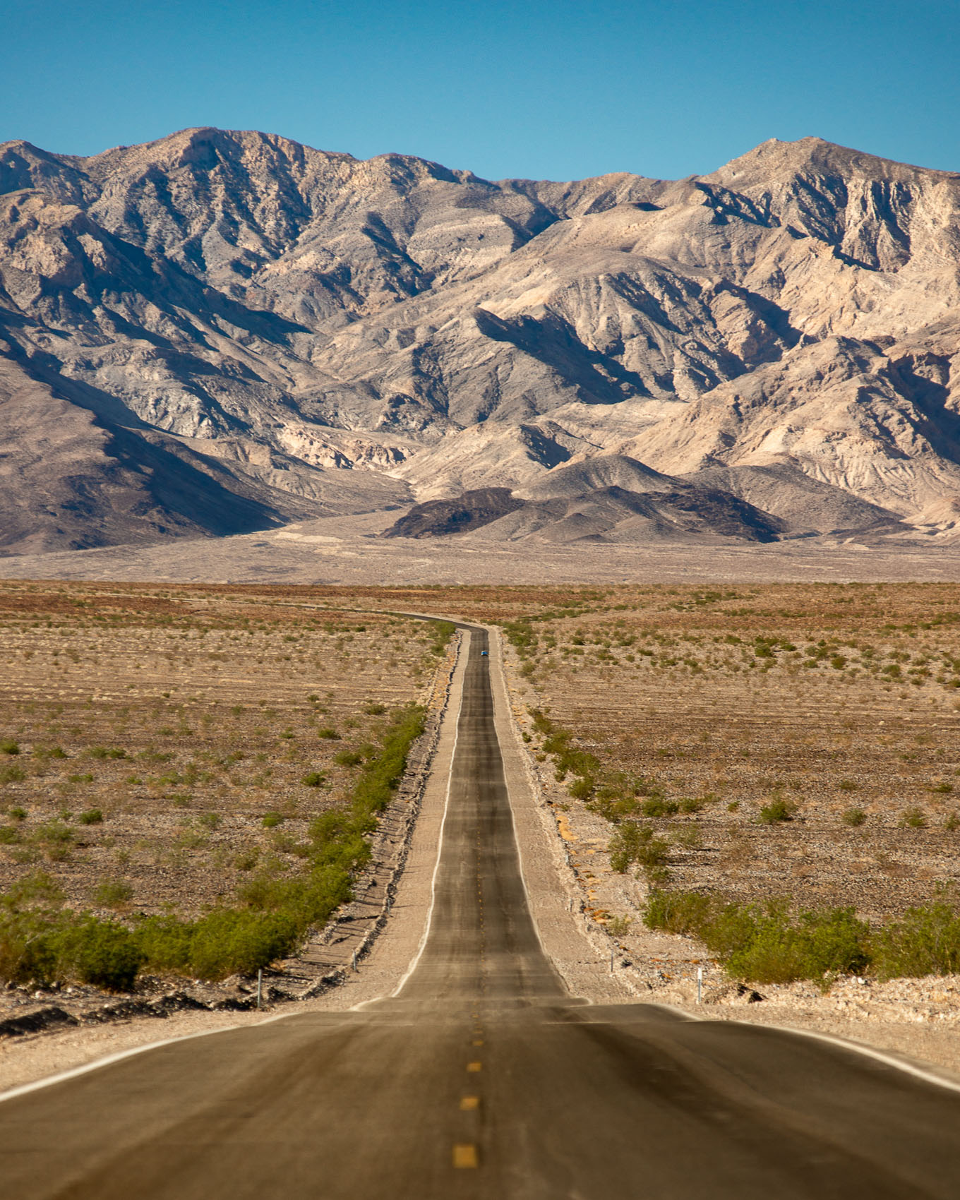 An empty desert road leading to mountains in Death Valley National Park.