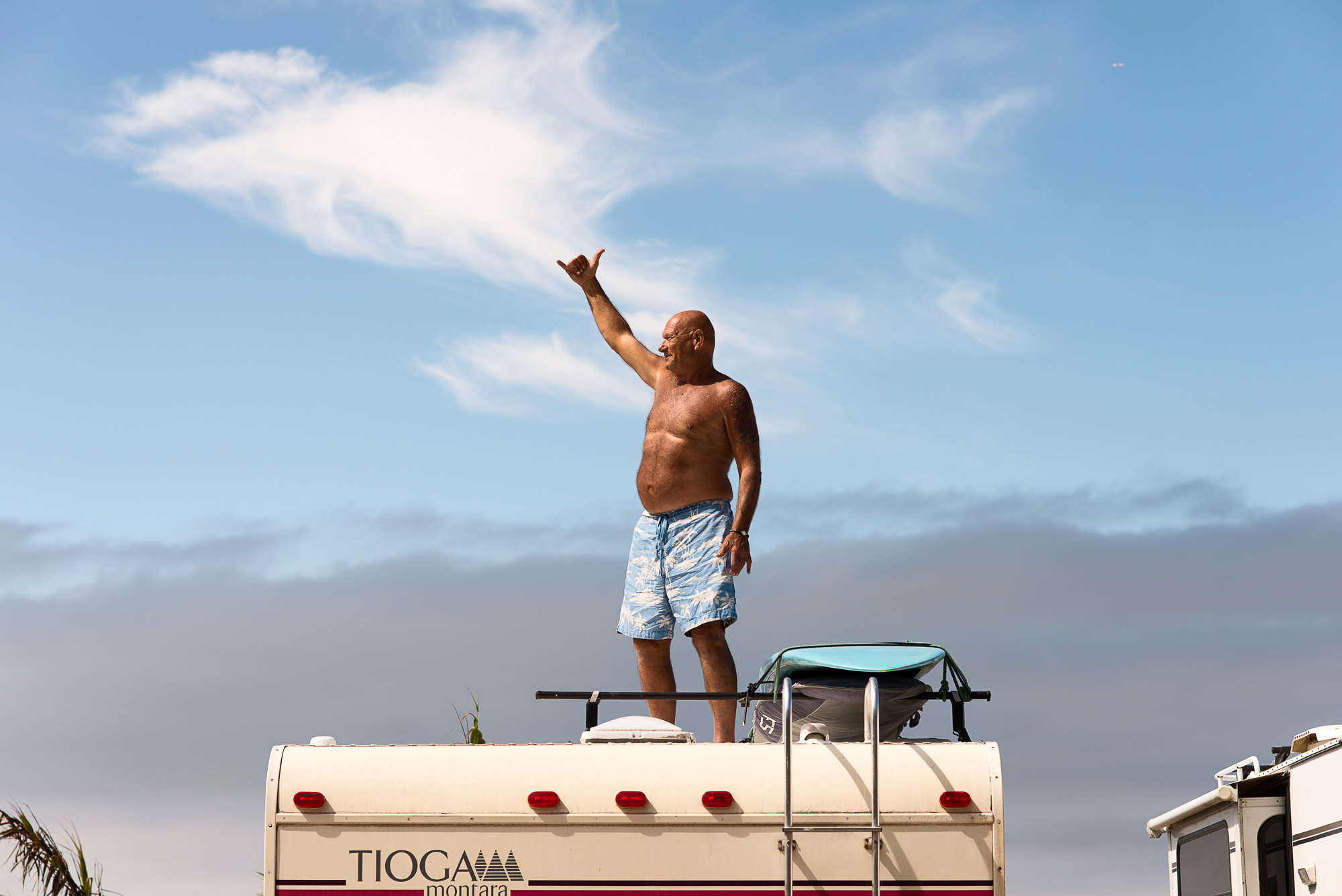 An older surfer signals hang loose atop his RV Camper in San Onofre, San Clemente, Calif.