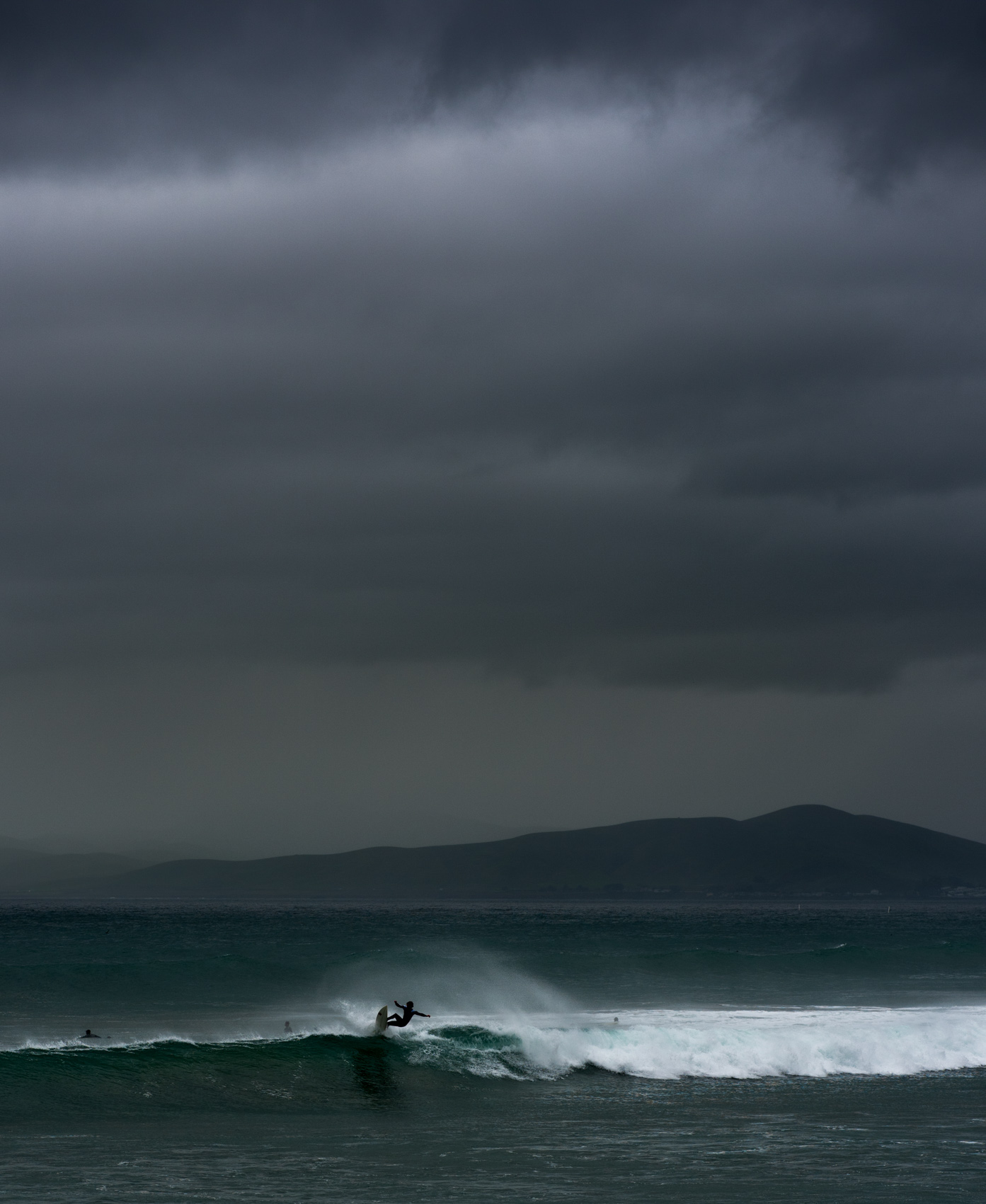 A surfer catches a wave under overcast skies as a rain storm approaches  in Morro Bay, Calif.