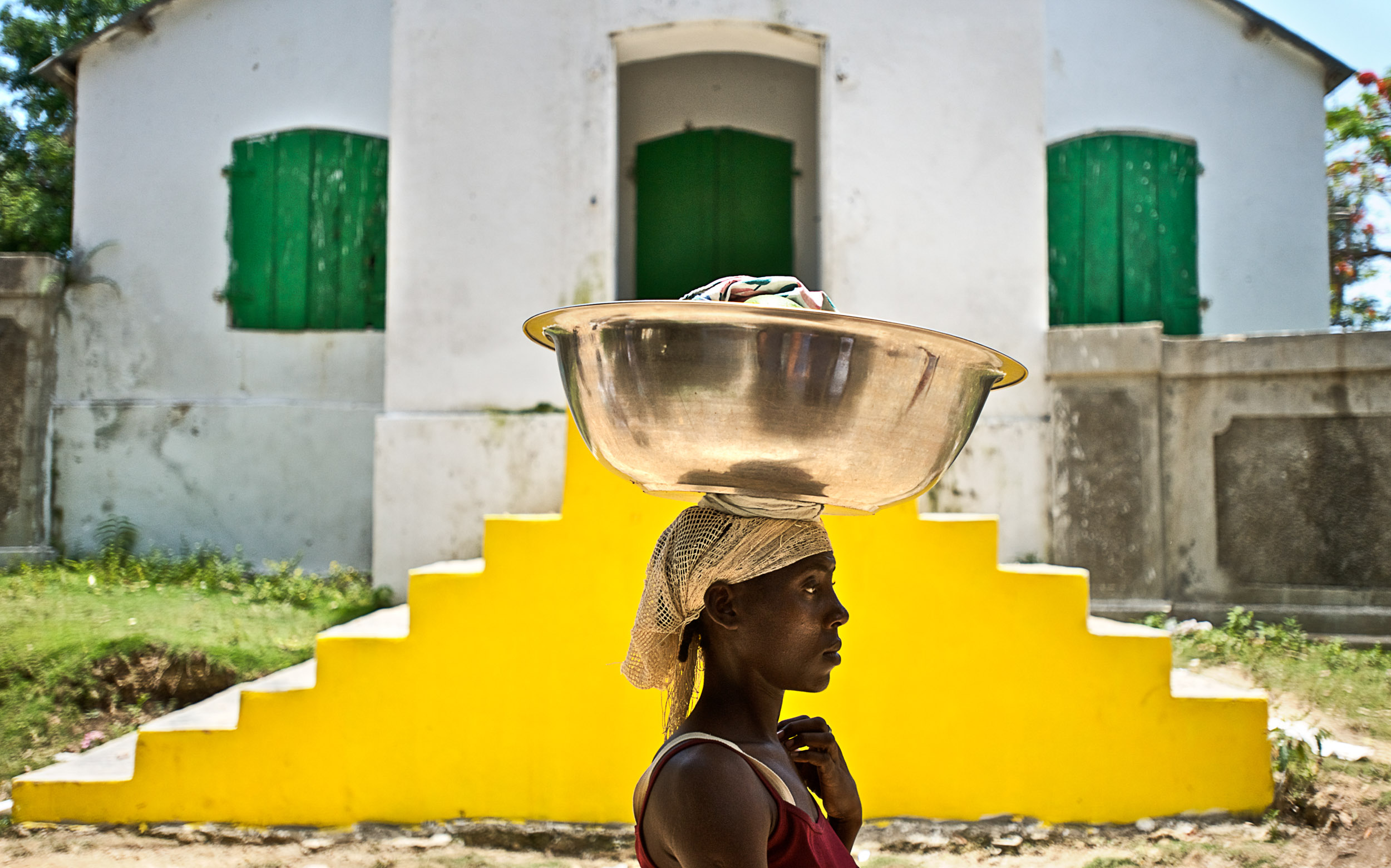 A woman walks past yellow stairs with a bowl on her head in Ville Bonheur, Haiti.