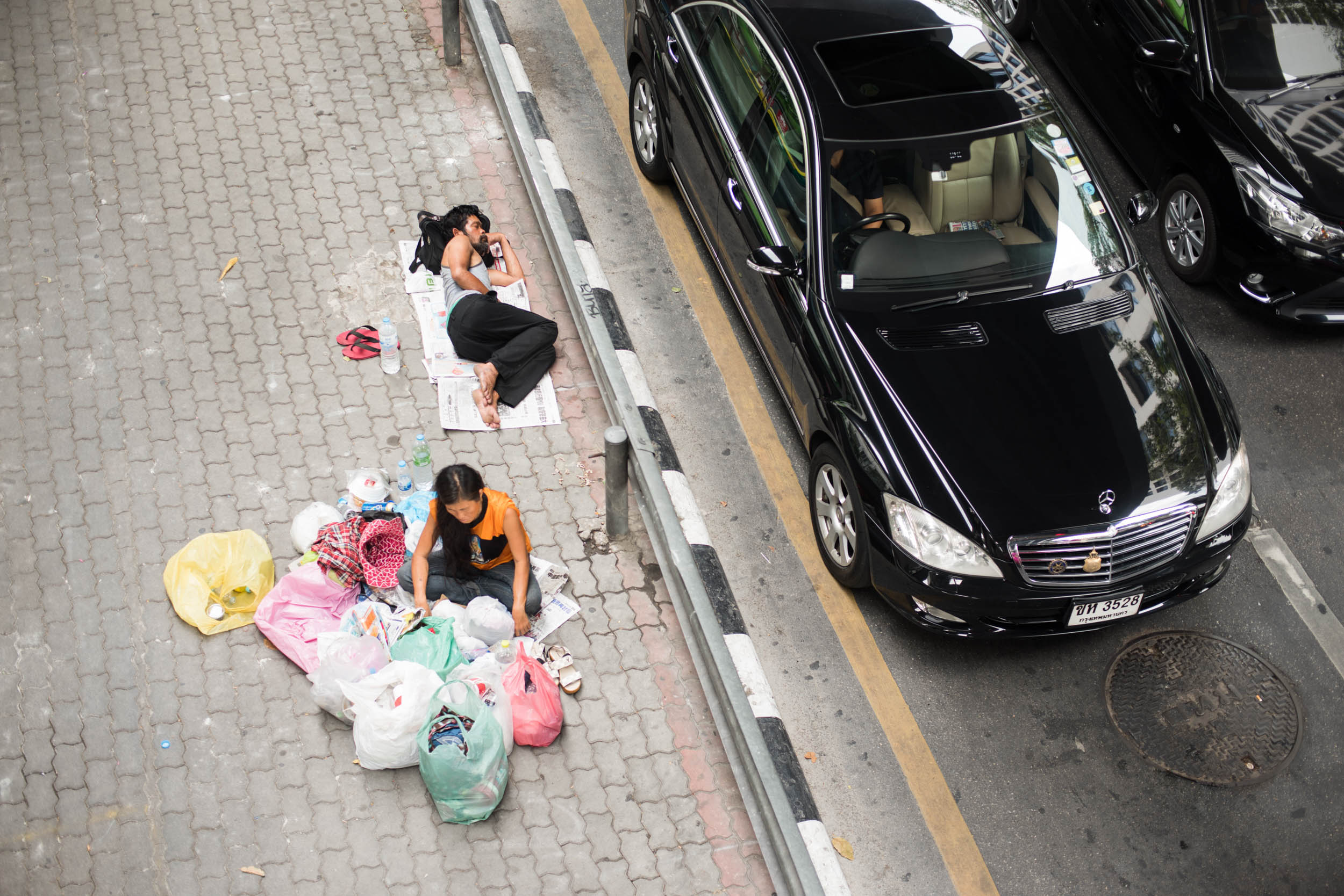 Homeless are juxtaposed with wealthy on streets of Bangkok, Thailand.