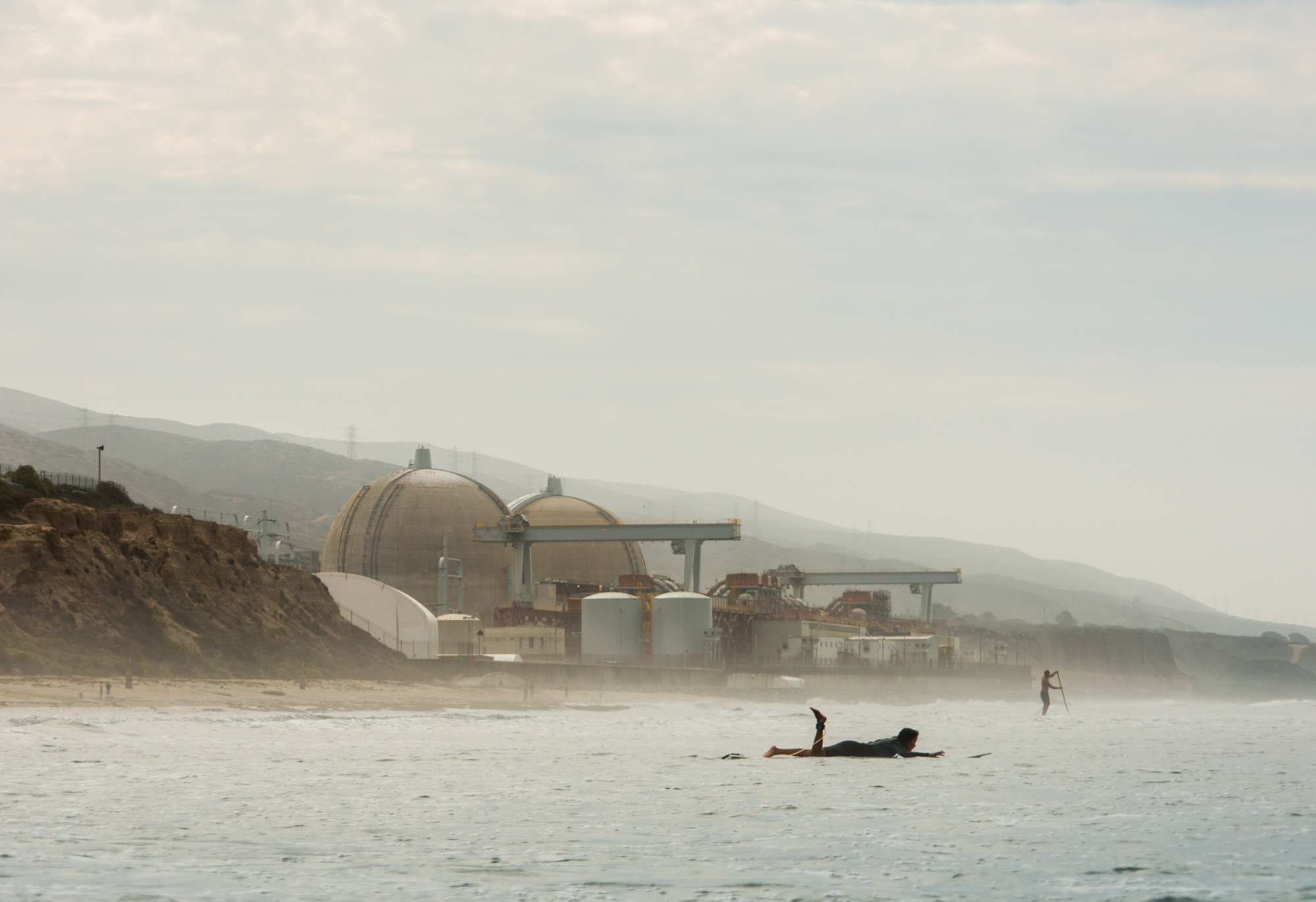A surfer paddles out in front of the San Onofre Nuclear Plant in San Clemente, Calif.