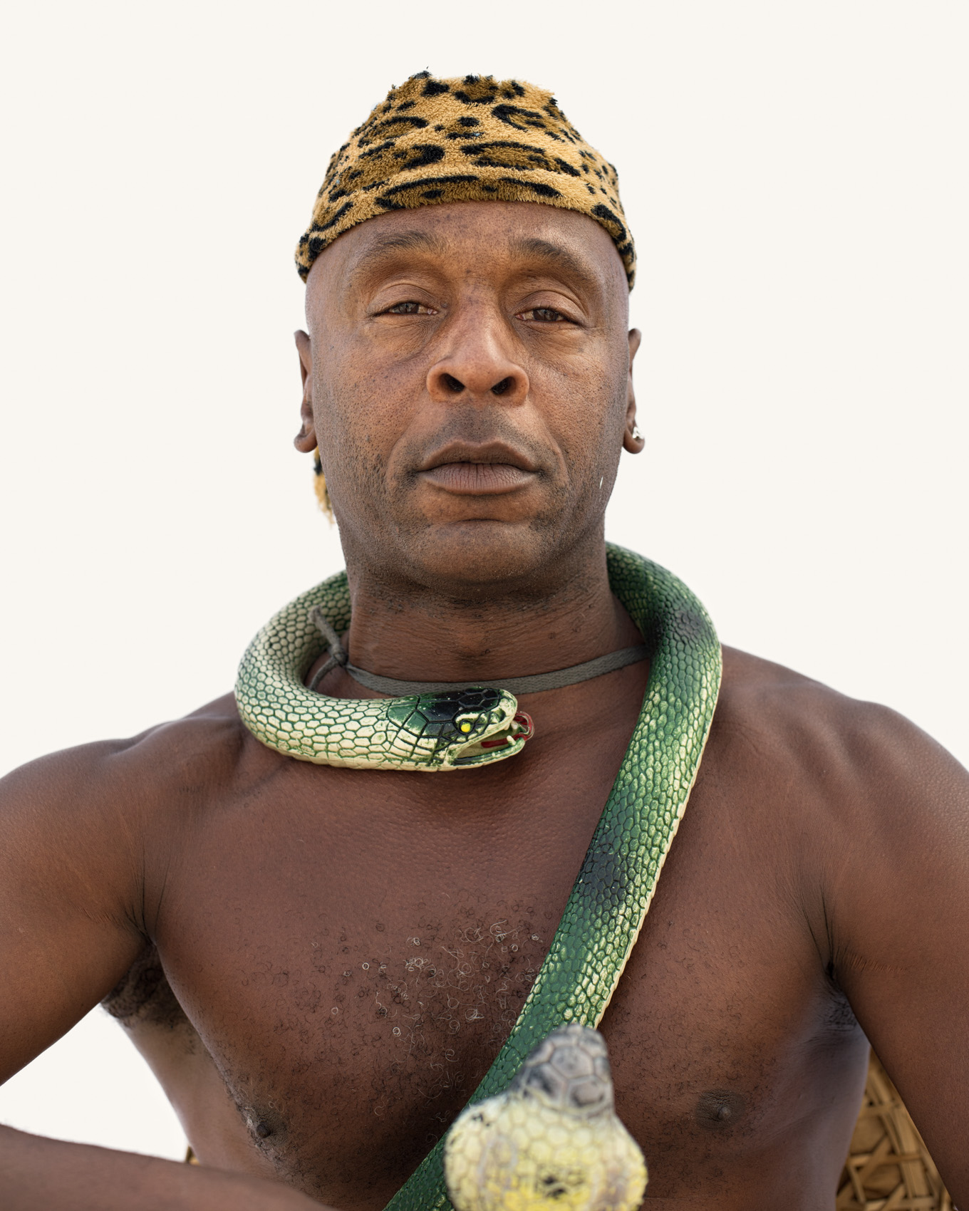 Man with snake around neck Venice Beach street portrait series on white backdrop.