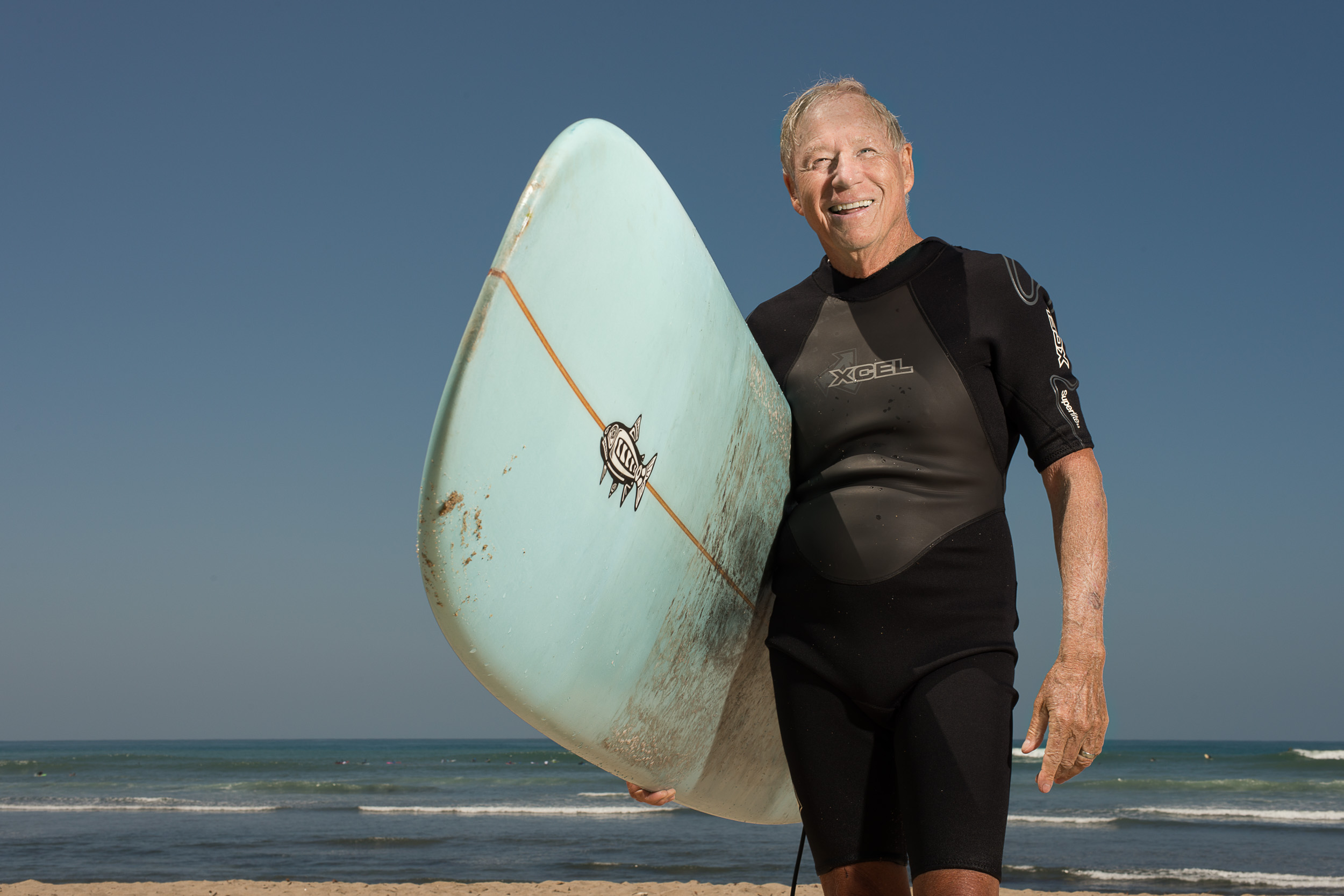 Senior surfer Mike McCaffrey portait with longboard on the beach at San Onofre.