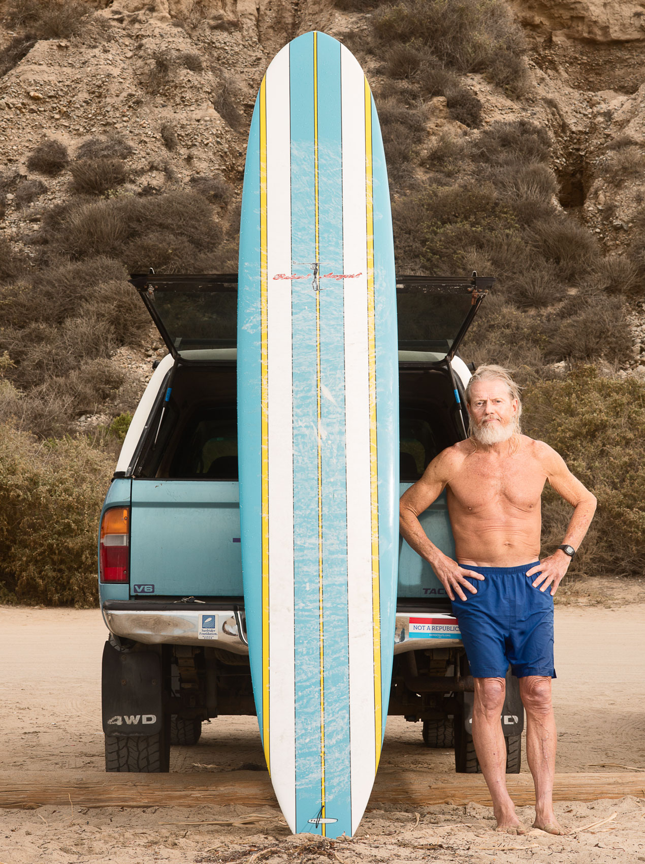 Senior surfer Bill Lyon portrait with his surfboard at San Onofre State Beach.