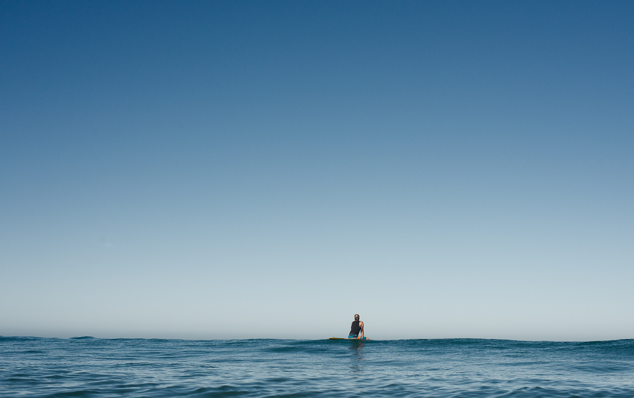 Older surfer John Moore waits for a wave in calm waters.
