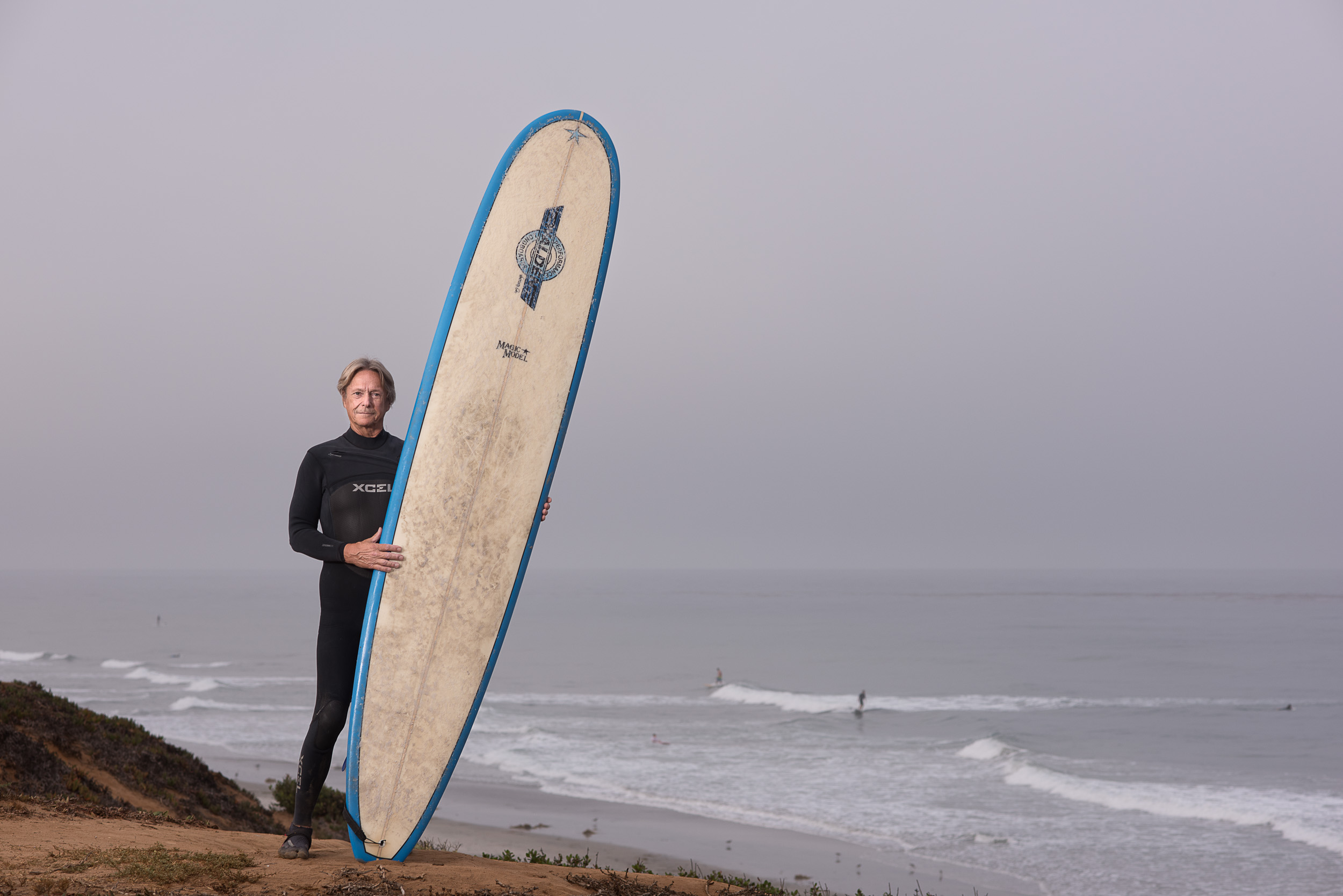 An older surfer portrait on a bluff overlooking the ocean.
