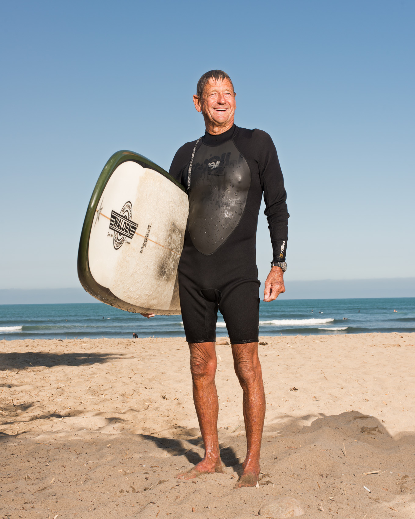 Older surfer Elroy Lang poses with his board on the beach at San Onofre State Beach.