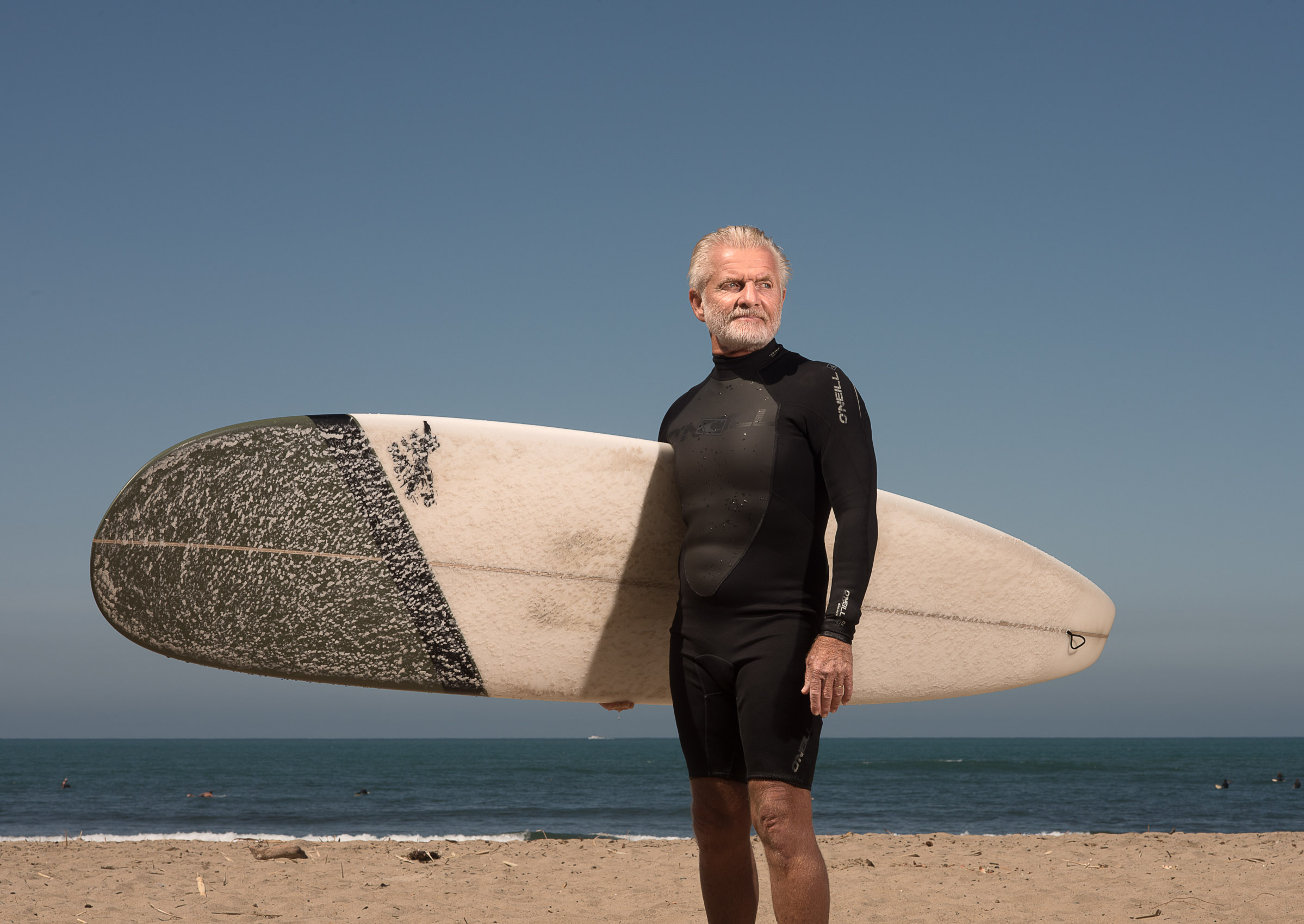 An older surfer poses for a portrait with his board at San Onofre State Beach.